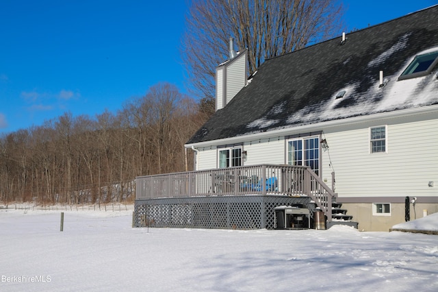 snow covered back of property with a deck and a chimney