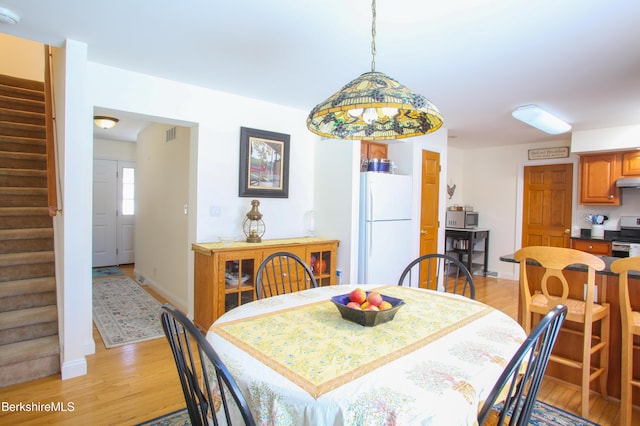 dining space featuring light wood-type flooring, visible vents, stairs, and baseboards