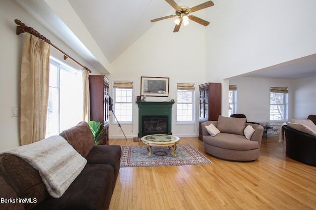 living room featuring hardwood / wood-style floors, a glass covered fireplace, ceiling fan, high vaulted ceiling, and baseboards