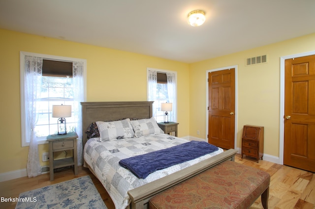 bedroom with light wood-style flooring, multiple windows, visible vents, and baseboards