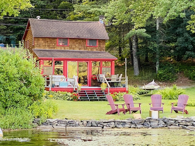 exterior space featuring a lawn, an outdoor fire pit, roof with shingles, and a deck with water view