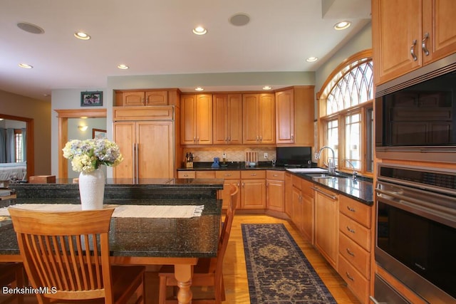 kitchen featuring backsplash, sink, light hardwood / wood-style flooring, built in appliances, and a kitchen island