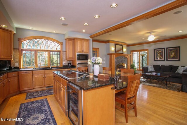 kitchen with backsplash, built in microwave, beverage cooler, a fireplace, and an island with sink