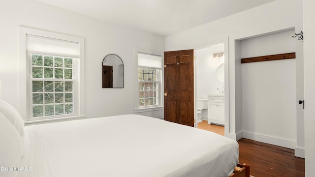 bedroom with ensuite bath, multiple windows, and hardwood / wood-style flooring