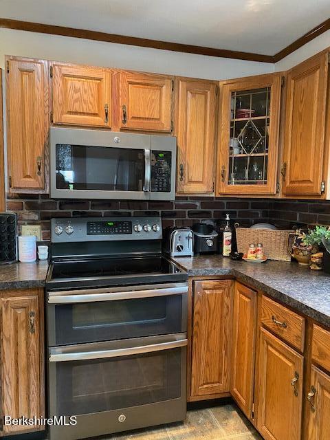16 Woodlawn Ave, North Adams, MA 01247 - kitchen with stainless steel appliances, dark countertops, brown cabinetry, decorative backsplash, and glass insert cabinets