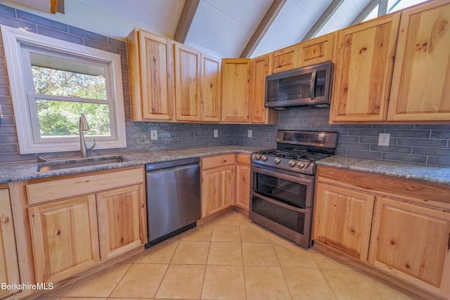 kitchen featuring light brown cabinets, vaulted ceiling with beams, tasteful backsplash, a sink, and stainless steel appliances