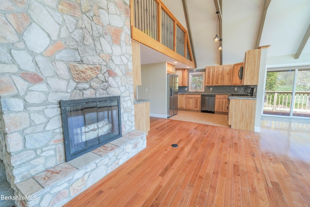 unfurnished living room with a stone fireplace, beam ceiling, high vaulted ceiling, baseboards, and light wood-style floors