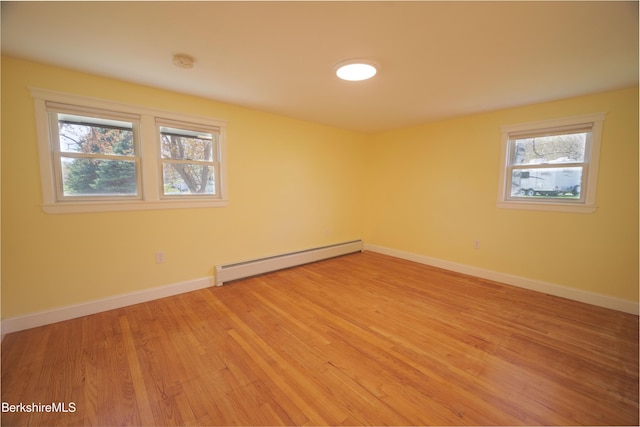 spare room featuring light wood-type flooring, a baseboard radiator, baseboards, and a healthy amount of sunlight