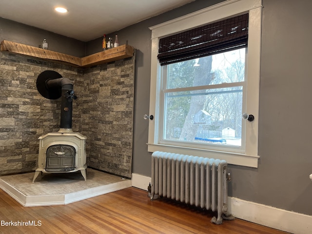 unfurnished living room featuring a wood stove, baseboards, radiator heating unit, and wood finished floors