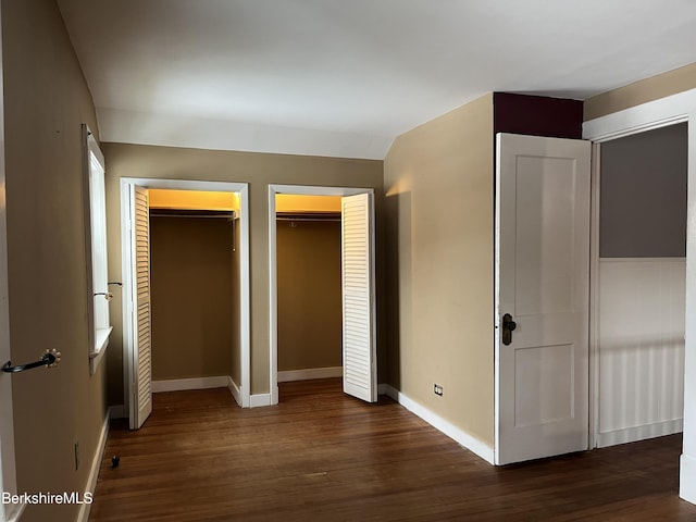 unfurnished bedroom featuring wood finished floors, two closets, and baseboards