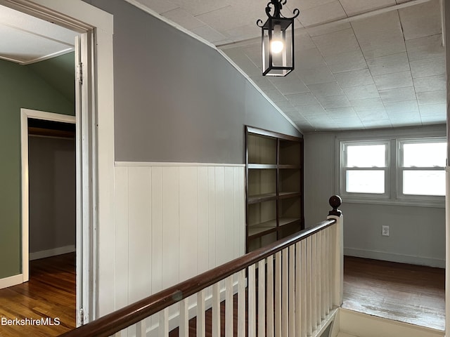 corridor featuring baseboards, vaulted ceiling, wood finished floors, and an upstairs landing