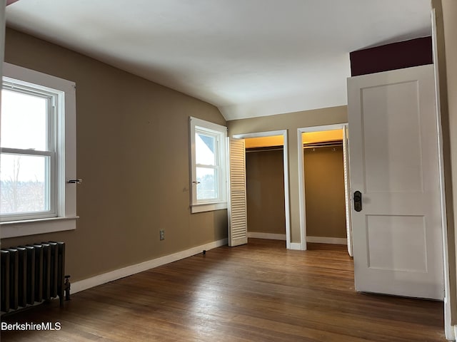 unfurnished bedroom featuring dark wood finished floors, multiple closets, radiator heating unit, vaulted ceiling, and baseboards