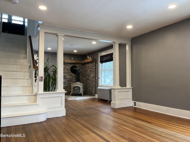 interior space featuring wood-type flooring, stairway, radiator heating unit, a wood stove, and ornate columns