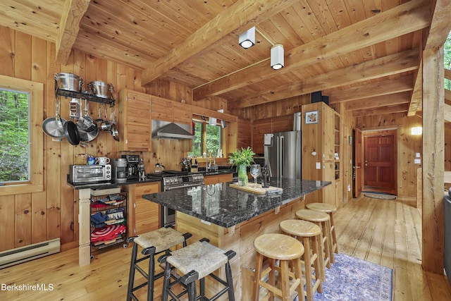 112 Silver St, Lanesborough, MA 01237 - kitchen featuring appliances with stainless steel finishes, wood walls, baseboard heating, wall chimney range hood, and light wood-style flooring