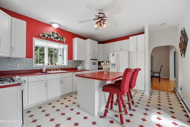 kitchen featuring arched walkways, a baseboard heating unit, white appliances, a sink, and light floors