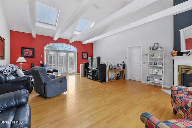 living room with wood finished floors, baseboards, french doors, lofted ceiling with skylight, and a glass covered fireplace