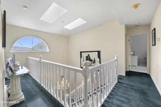 hall featuring a skylight, baseboards, carpet flooring, and an upstairs landing