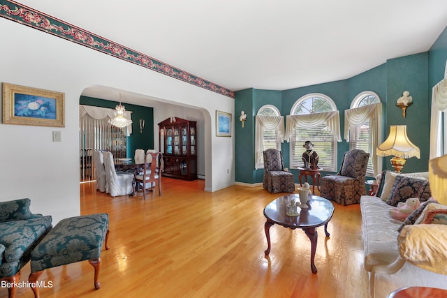 living area with arched walkways, baseboards, wood finished floors, and an inviting chandelier