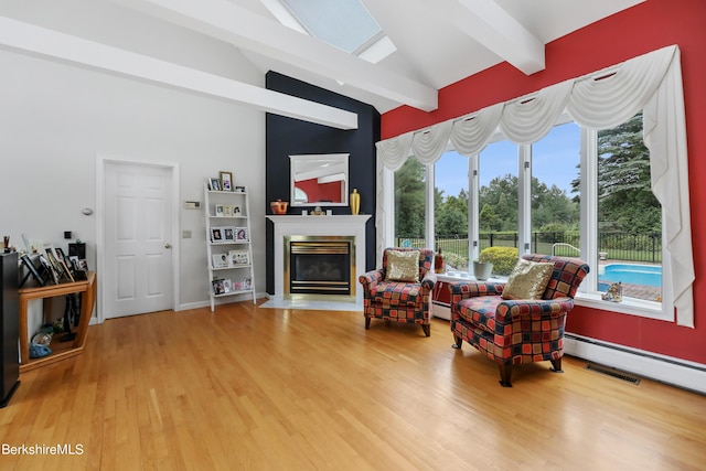 sitting room with vaulted ceiling with beams, baseboard heating, wood finished floors, and a glass covered fireplace