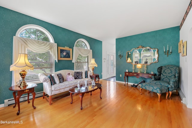 living area with an accent wall, a baseboard radiator, wood finished floors, and baseboards