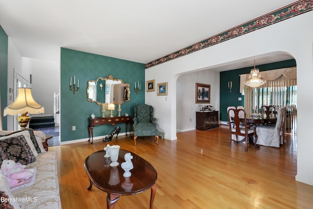 living area with arched walkways, a chandelier, wood finished floors, baseboards, and stairway