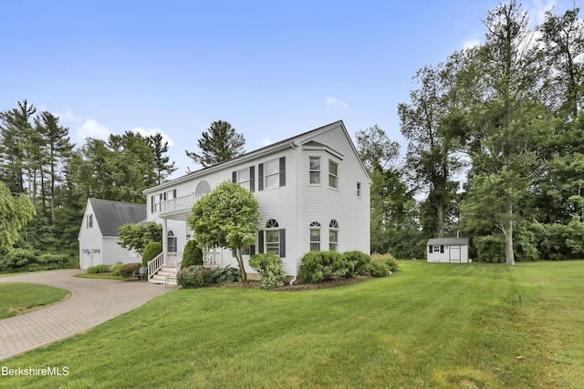 colonial inspired home featuring decorative driveway, an outdoor structure, a front lawn, and a shed