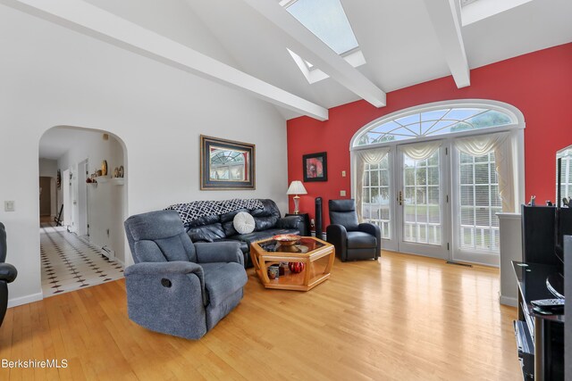 living area featuring arched walkways, beam ceiling, a skylight, french doors, and wood finished floors