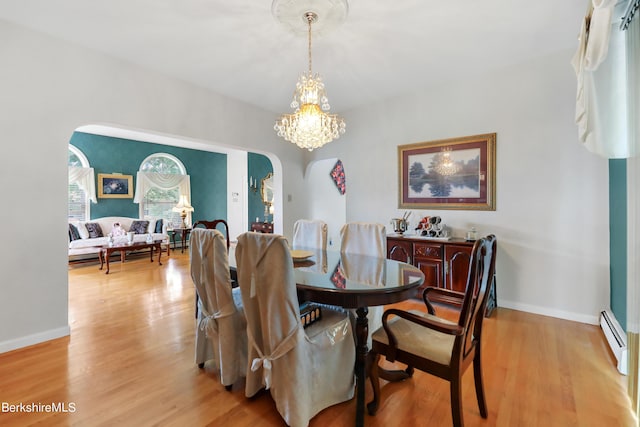 dining space with arched walkways, light wood-type flooring, a baseboard radiator, and baseboards