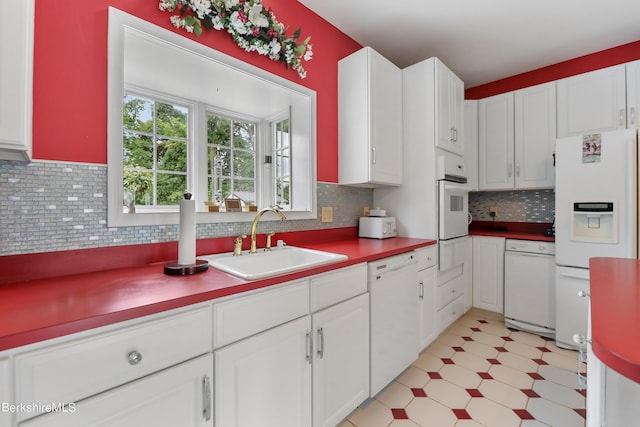 kitchen with light floors, tasteful backsplash, white cabinetry, a sink, and white appliances