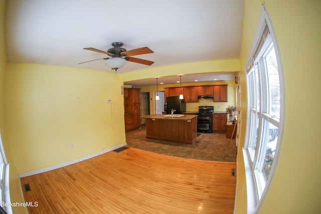 kitchen featuring ceiling fan, black appliances, pendant lighting, hardwood / wood-style floors, and an island with sink