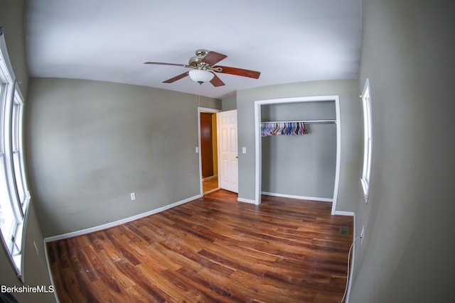 unfurnished bedroom with ceiling fan, dark hardwood / wood-style floors, multiple windows, and a closet