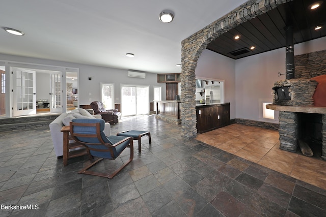 living area with a wall mounted AC, decorative columns, stone tile flooring, and a stone fireplace