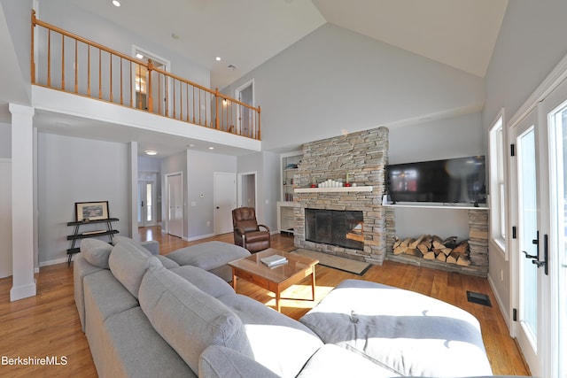 living room featuring a stone fireplace, wood finished floors, visible vents, baseboards, and decorative columns