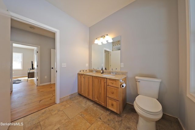 bathroom with double vanity, a sink, toilet, and baseboards