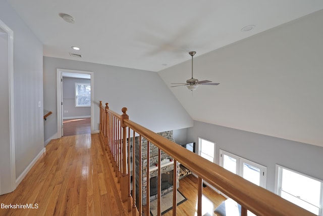 hall with light wood-style flooring, visible vents, an upstairs landing, vaulted ceiling, and baseboards