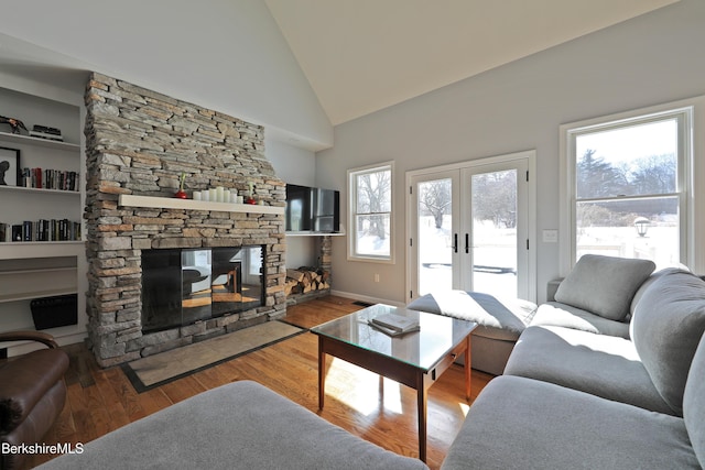 living area featuring high vaulted ceiling, a fireplace, wood finished floors, baseboards, and french doors