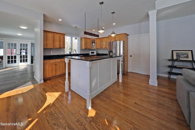 kitchen with dark wood finished floors, stainless steel refrigerator with ice dispenser, decorative columns, dark countertops, and brown cabinetry