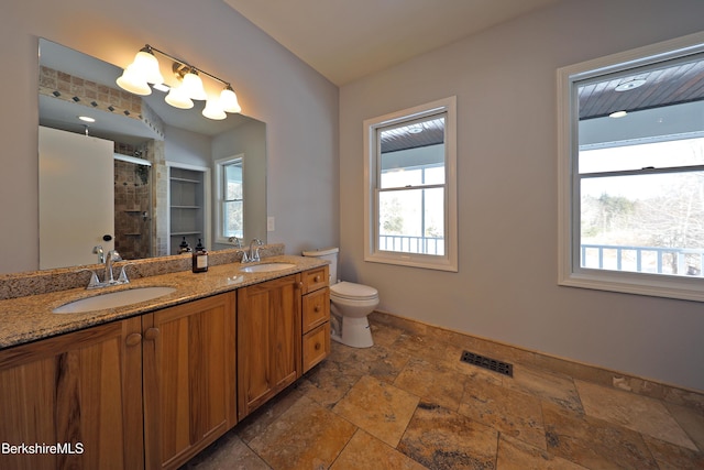 full bathroom with stone tile flooring, visible vents, a sink, and a shower stall