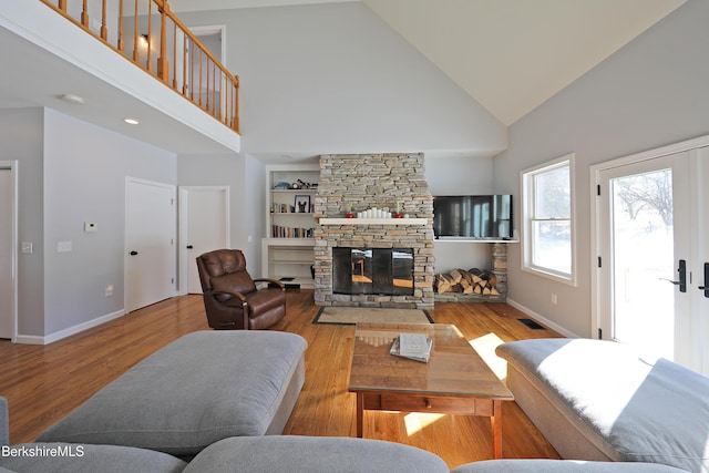 living room featuring baseboards, visible vents, wood finished floors, a stone fireplace, and high vaulted ceiling