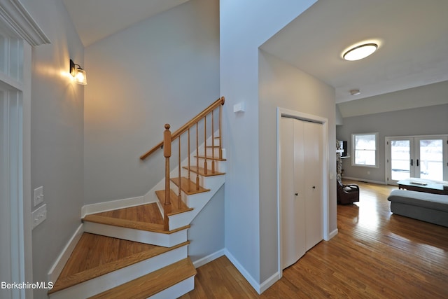 staircase with french doors, vaulted ceiling, baseboards, and wood finished floors