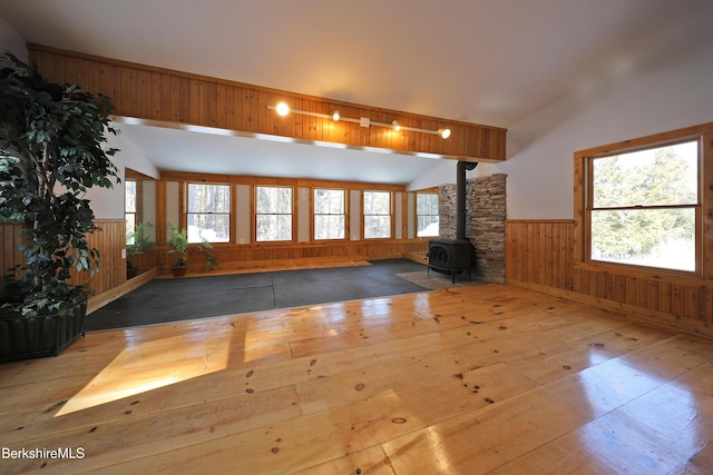 unfurnished living room with a wainscoted wall, wood-type flooring, rail lighting, a wood stove, and wooden walls