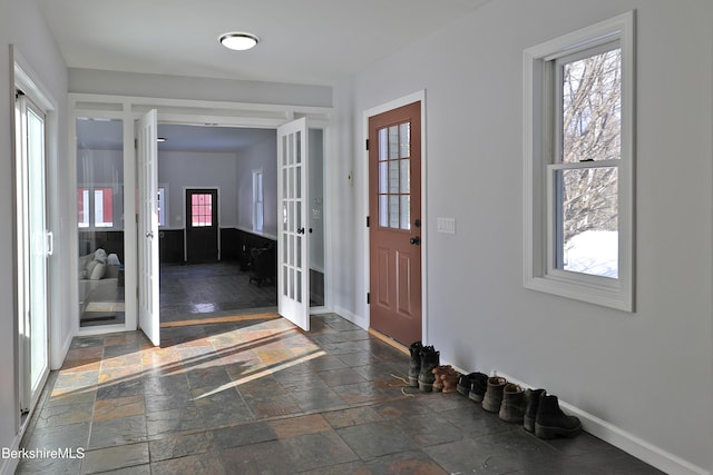 foyer with stone tile floors, baseboards, and french doors