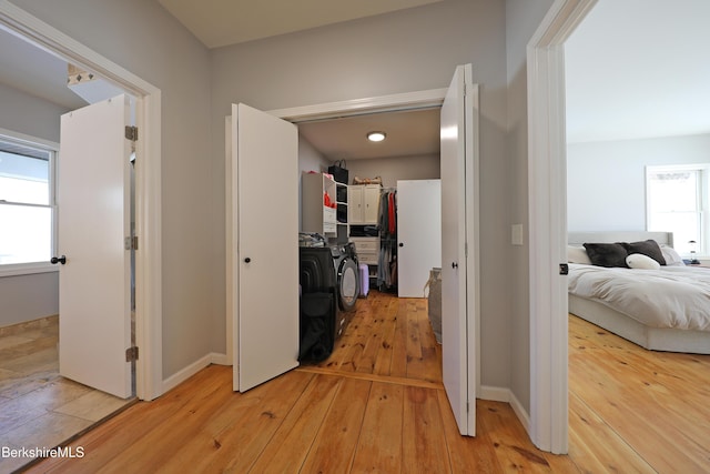 hall with light wood-type flooring, baseboards, and washing machine and clothes dryer