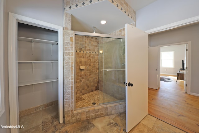 bathroom featuring baseboards, a spacious closet, a stall shower, and stone finish flooring