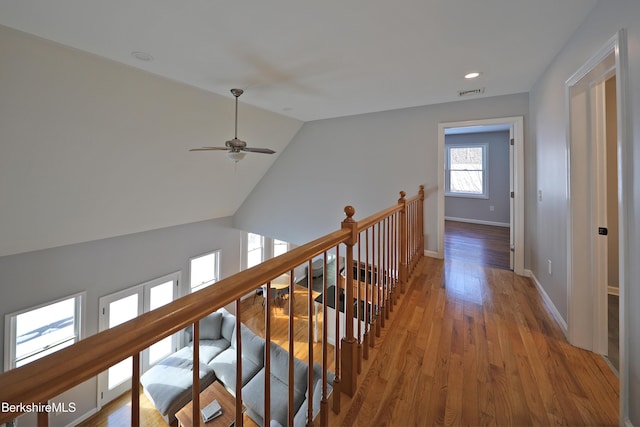 hallway featuring visible vents, baseboards, wood finished floors, vaulted ceiling, and an upstairs landing