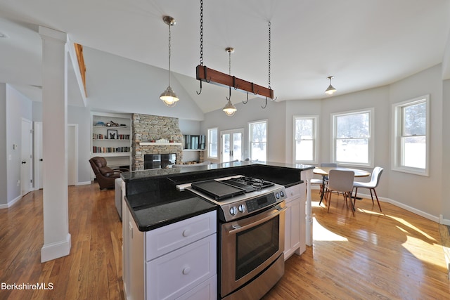 kitchen featuring dark countertops, vaulted ceiling, light wood-type flooring, stainless steel range with gas cooktop, and white cabinetry