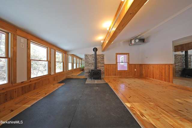 unfurnished living room featuring a wainscoted wall, a wealth of natural light, wood walls, and a wood stove