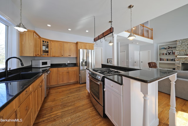 kitchen with dark wood finished floors, stainless steel appliances, glass insert cabinets, open floor plan, and a sink