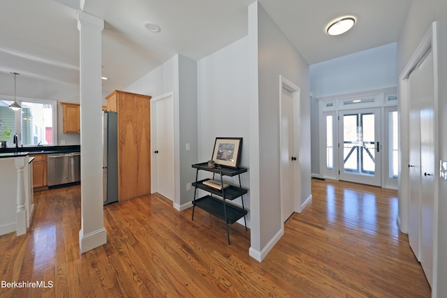 hall with baseboards, a sink, ornate columns, and wood finished floors