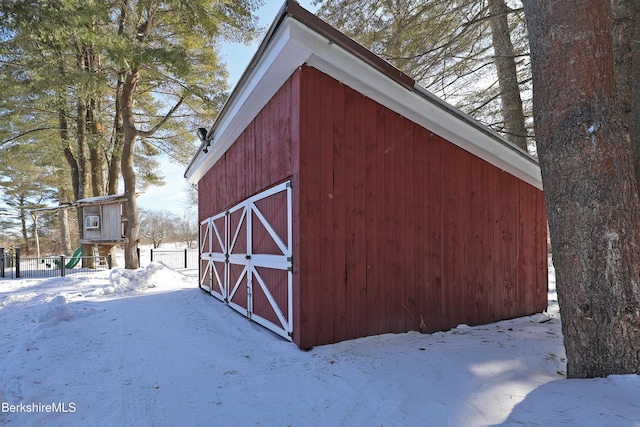 snow covered structure featuring a barn, fence, and an outbuilding